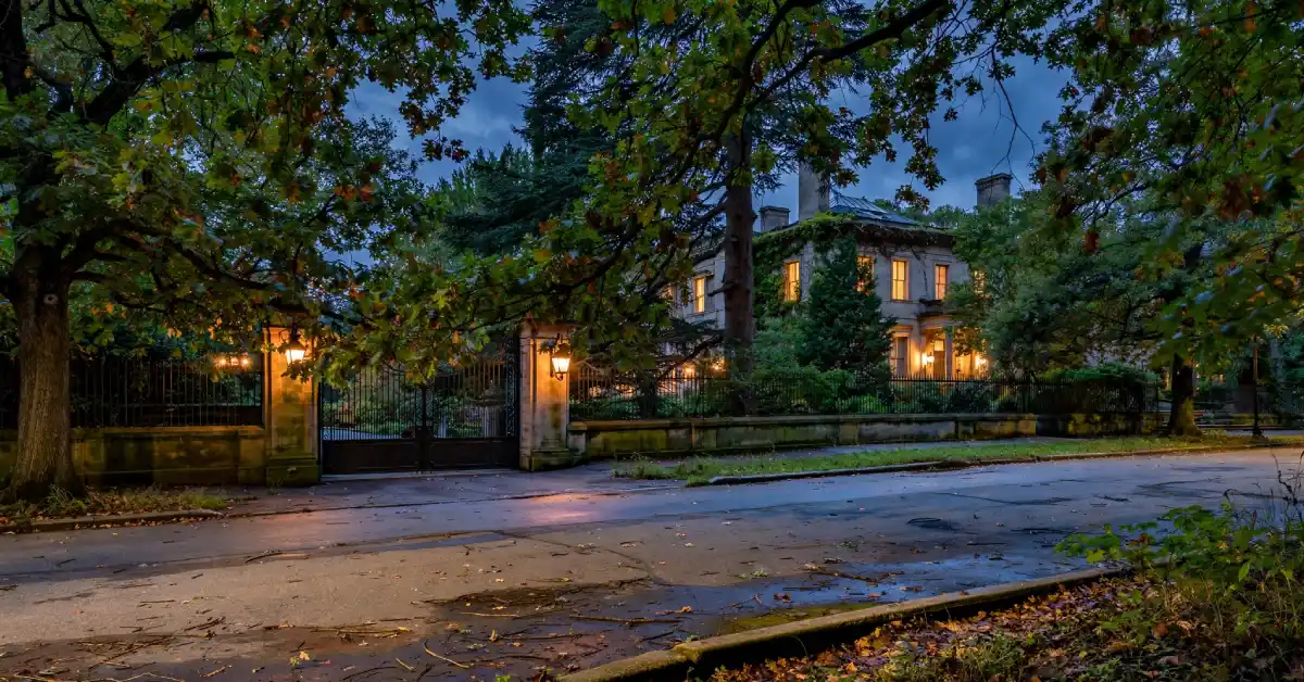 Gated Preston Hollow mansion partially visible through trees at dusk