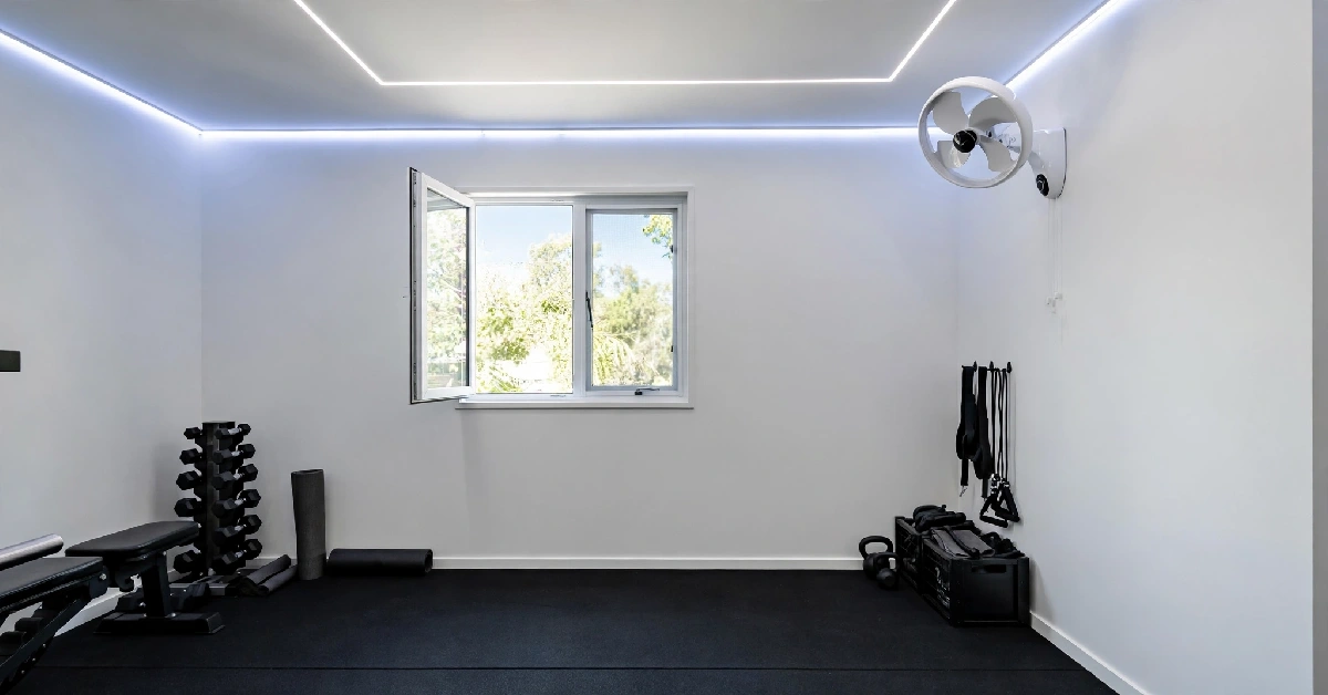 Home gym with natural light from an open window, a wall fan, and LED ceiling lighting